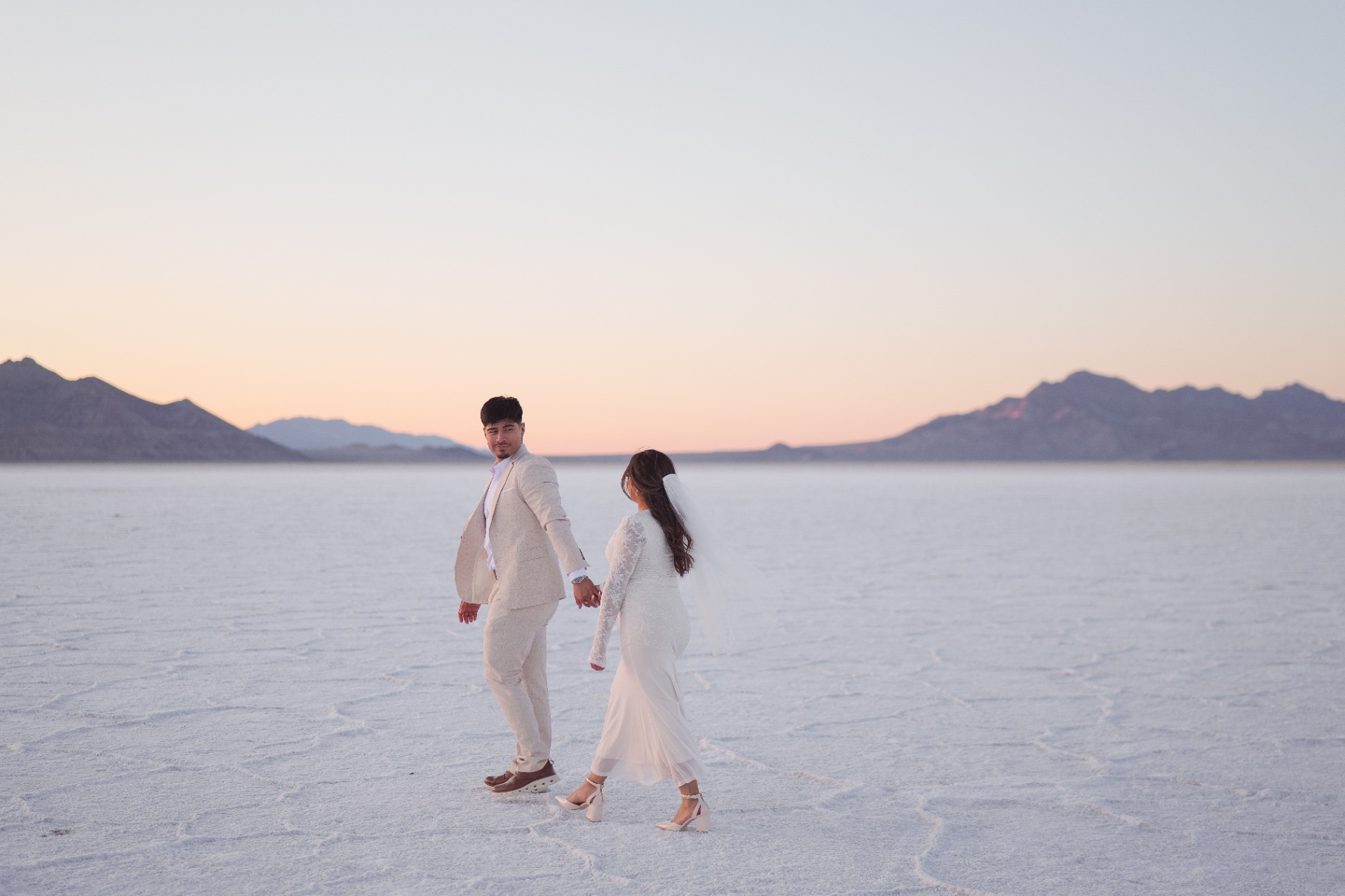 Bride and groom walking hand in hand on the salt flats at dusk