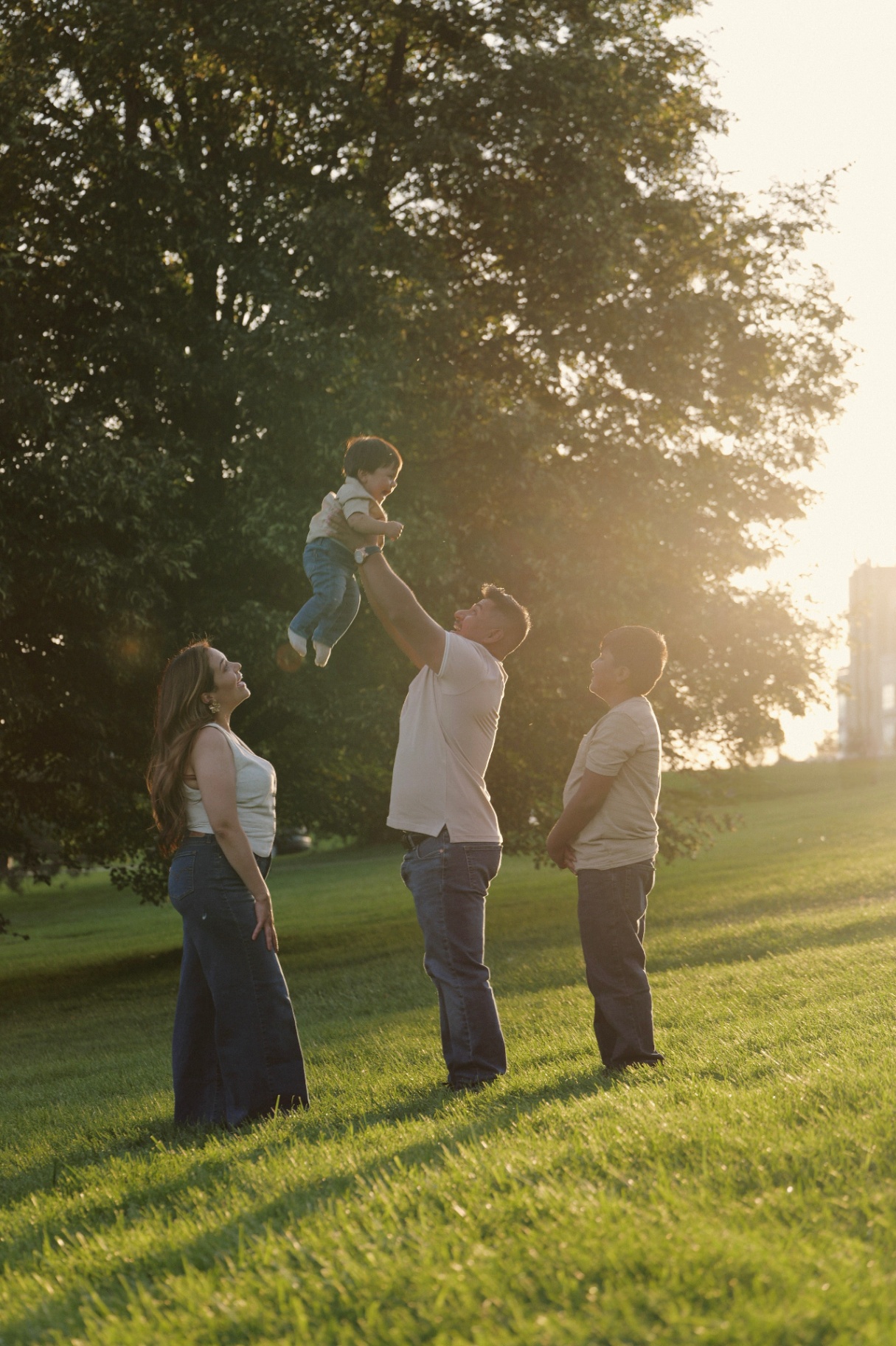Father tossing baby in the air at golden hour with family