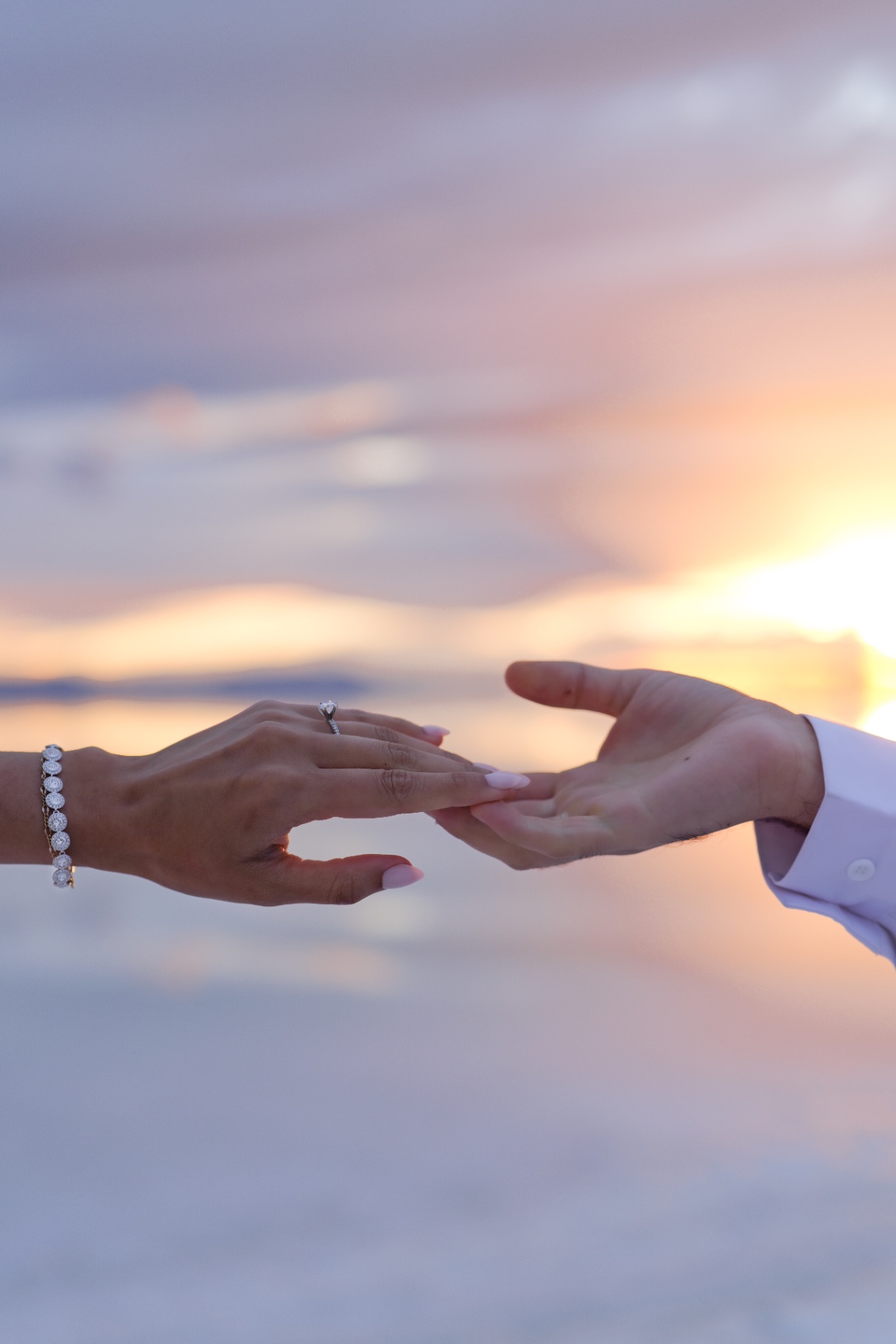 Hands and engagement ring against a pastel sunset
