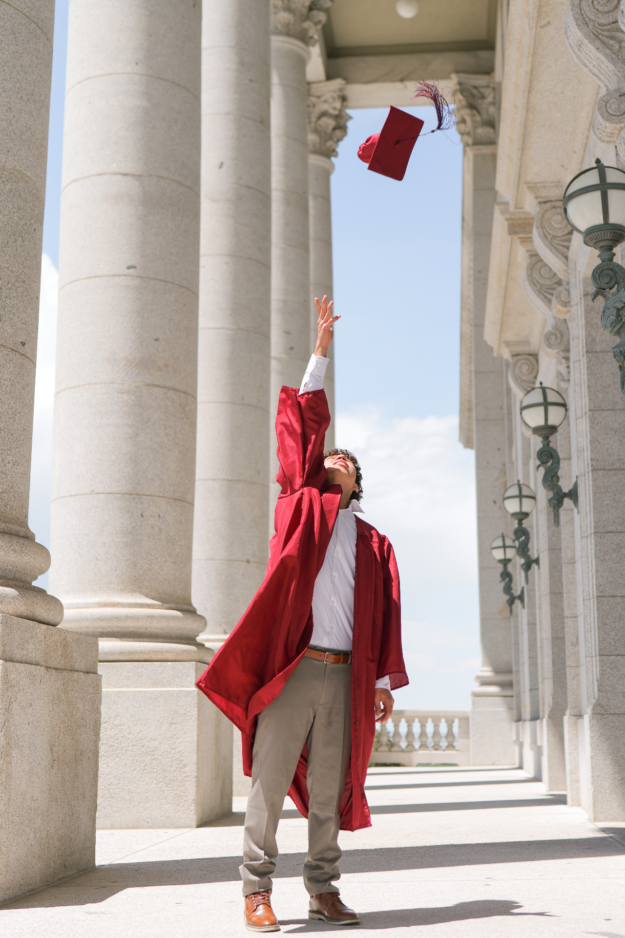 Graduate tossing a red cap between marble columns