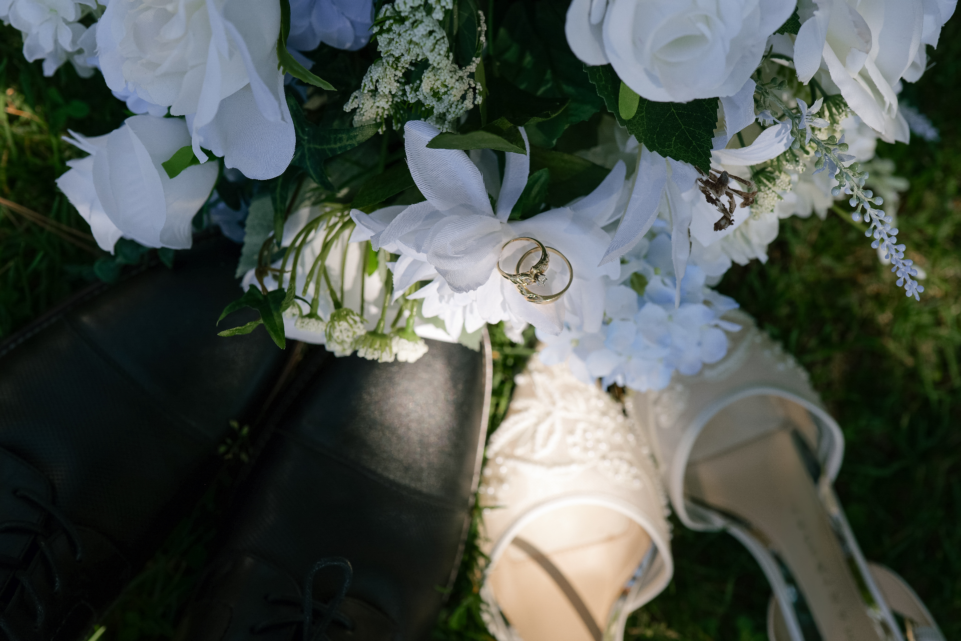 Wedding rings on a bouquet beside bridal shoes